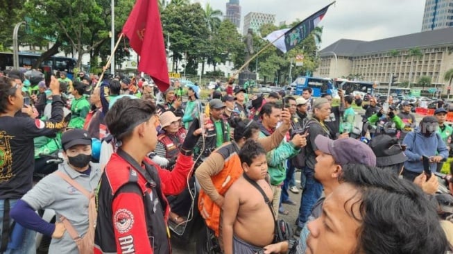 Penampakan sejumlah elemen komunitas ojek online (ojol) menggelar aksi unjuk rasa di depan Patung Kuda Arjuna Wijaya, Gambir, Jakarta Pusat (Jakarta Pusat) pada Selasa (20/5/2025). (Suara.com/Fakhri Fuadi)