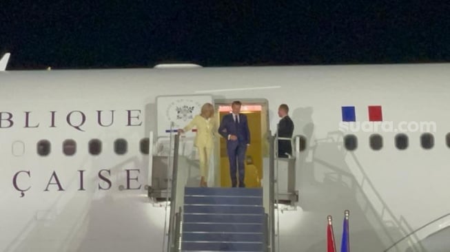 Presiden Prancis Emmanuel Macron tiba di Lapangan Udara (Lanud) Halim Perdanakusuma, Jakarta, serelah sebelumnya lepas landas dari Hanoi, Vietnam. Presiden Macron juga tampak menggandeng istrinya, Brigitte Macron saat turun dari pesawat kepresidenan. (Suara.com/Novian Ardiansyah)