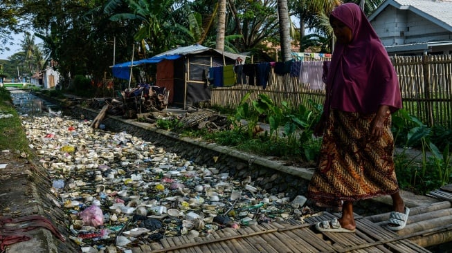 Seorang warga berjalan diatas saluran irigasi yang dipenuhi sampah di Desa Susukan, Kabupaten Seran, Banten, Senin (2/6/2025). [ANTARA FOTO/Muhammad Bagus Khoirunas/bar]