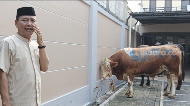 Ayaqh Ayu Ting Ting, Abdul Rozak bersama sapi kurban keluarga di rumahnya yang berada di kawasan Depok, Jawa Barat pada Jumat, 6 Juni 2025. [Suara.com/Rena Pangesti]