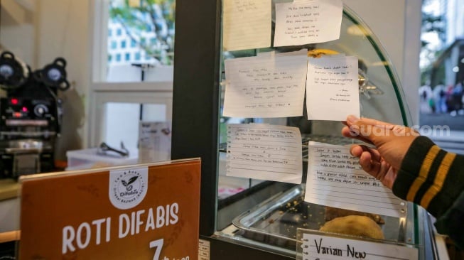 Pelanggan menempelkan pesanannya di Kopi Difabis, Terowongan Kendal, Jakarta, (9/6/2025). [Suara.com/Alfian Winanto]