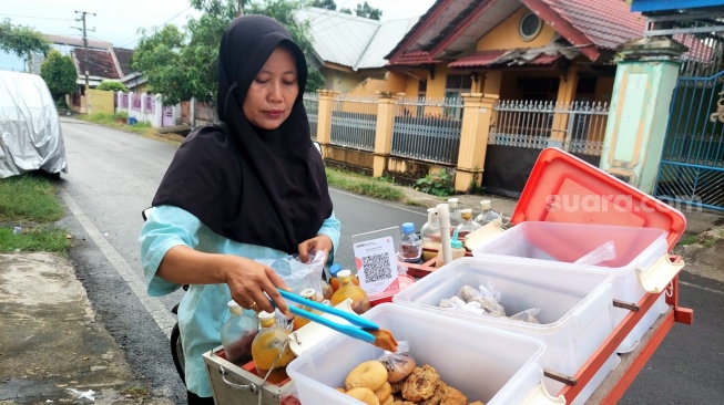 Puji Lestari (50) Penjual jamu keliling telah menggantungkan hidupnya dari ramuan tradisional kini menggunakan QRIS untuk pembayaran [SuaraSulsel.id/Lorensia Clara]