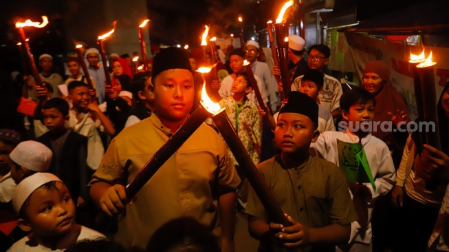 Sejumlah warga mengikuti pawai obor di RW 08 Kelurahan Menteng, Jakarta, Kamis (26/6/2025). [Suara.com/Alfian Winanto]