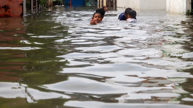 Warga beraktivitas di tengah banjir yang melanda di Jalan Tipala, Makasar, Jakarta Timur, Senin (7/7/2025). [Suara.com/Alfian Winanto]