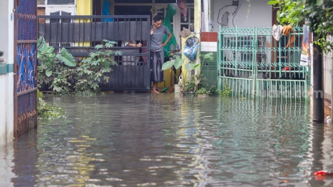 Warga beraktivitas di tengah banjir yang melanda di Jalan Tipala, Makasar, Jakarta Timur, Senin (7/7/2025). [Suara.com/Alfian Winanto]