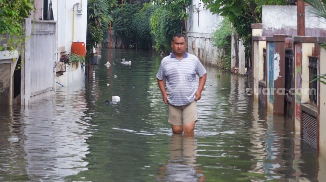 Warga beraktivitas di tengah banjir yang melanda di Jalan Tipala, Makasar, Jakarta Timur, Senin (7/7/2025). [Suara.com/Alfian Winanto]