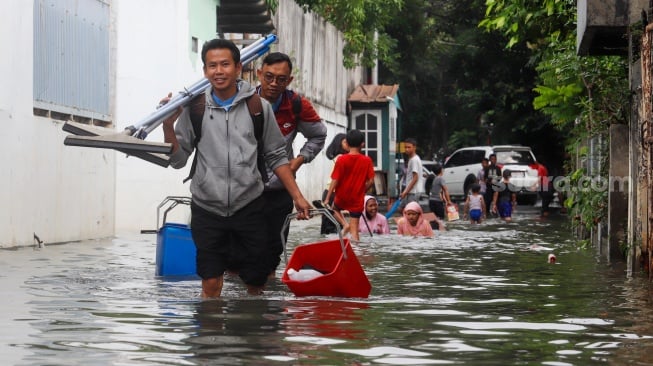 Warga beraktivitas di tengah banjir yang melanda di Jalan Tipala, Makasar, Jakarta Timur, Senin (7/7/2025). [Suara.com/Alfian Winanto]