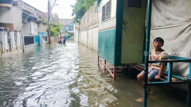 Warga beraktivitas di tengah banjir yang melanda di Jalan Tipala, Makasar, Jakarta Timur, Senin (7/7/2025). [Suara.com/Alfian Winanto]