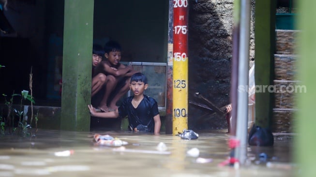 Warga beraktivitas di tengah banjir yang melanda pemukiman padat penduduk di kawasan Kebon Pala, Kampung Melayu, Jakarta, Selasa (8/7/2025). [Suara.com/Alfian Winanto]