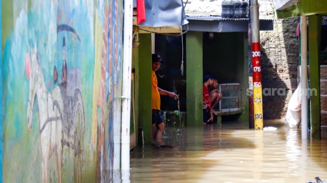 Warga beraktivitas di tengah banjir yang melanda pemukiman padat penduduk di kawasan Kebon Pala, Kampung Melayu, Jakarta, Selasa (8/7/2025). [Suara.com/Alfian Winanto]