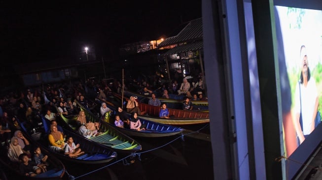 Sejumlah warga menonton bioskop terapung dari perahunya di Desa Muara Enggelam, Muara Wis, Kutai Kartanegara, Kalimantan Timur, Selasa (22/7/2025). [ANTARA FOTO/M Risyal Hidayat/tom]
