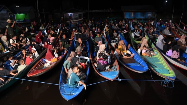 Sejumlah warga menonton bioskop terapung dari perahunya di Desa Muara Enggelam, Muara Wis, Kutai Kartanegara, Kalimantan Timur, Selasa (22/7/2025). [ANTARA FOTO/M Risyal Hidayat/tom]