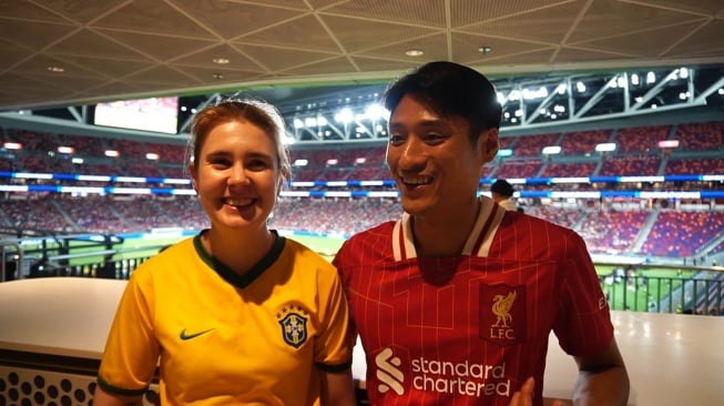Dua pendukung Liverpool Calvin dan Bruna antusias menonton sesi latihan terbuka Liverpool di Kai Tak Stadium, Kwoloon, Hong Kong pada Kamis (24/7/2024) sore waktu setempat [Suara.com/Arief Apriadi]