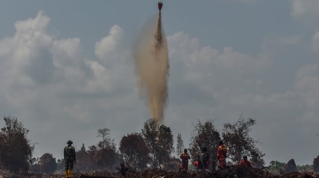 Sejumlah petugas menyaksikan helikopter water bombing VN8416 milik BNPB menjatuhkan air saat memadamkan api kebakaran hutan dan lahan (karhutla) di lahan gambut Desa Gambut Jaya, Muaro Jambi, Jambi, Rabu (30/7/2025). [ANTARA FOTO/Wahdi Septiawan/foc]