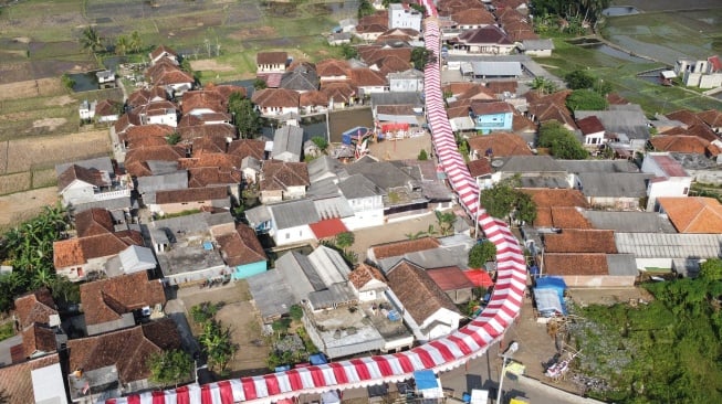 Foto udara kain merah putih terpasang di jalan Kampung Cibahong, Desa Sukamenak, Kecamatan Sukarame, Kabupaten Tasikmalaya, Jawa Barat, Rabu (6/8/2025). [ANTARA FOTO/Adeng Bustomi/tom]