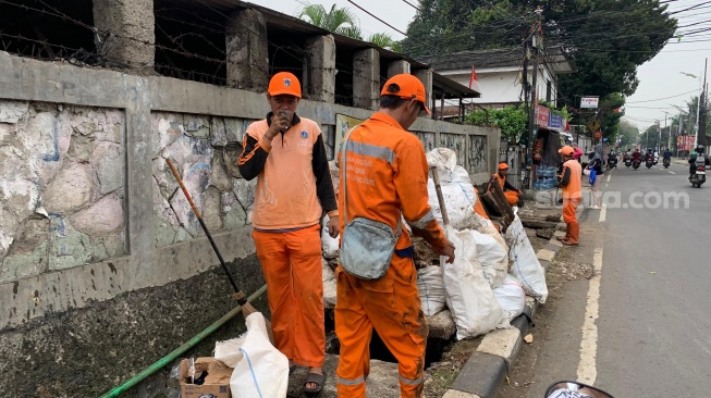Pekerja Penanganan Prasarana dan Sarana Umum (PPSU) atau pasukan oranye tengah mengeruk sampah dan kotoran dari saluran got. (Suara.com/Maylaffayza Adinda Hollaoena)