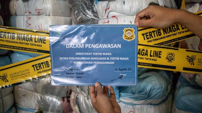 Petugas menempelkan tanda pengawasan pada barang bukti pakaian bekas saat ekspose hasil pengawasan barang impor tidak sesuai ketentuan oleh Kementerian Perdagangan di Bojongsoang, Kabupaten Bandung, Jawa Barat, Selasa (19/8/2025). [ANTARA FOTO/Abdan Syakura/rwa]