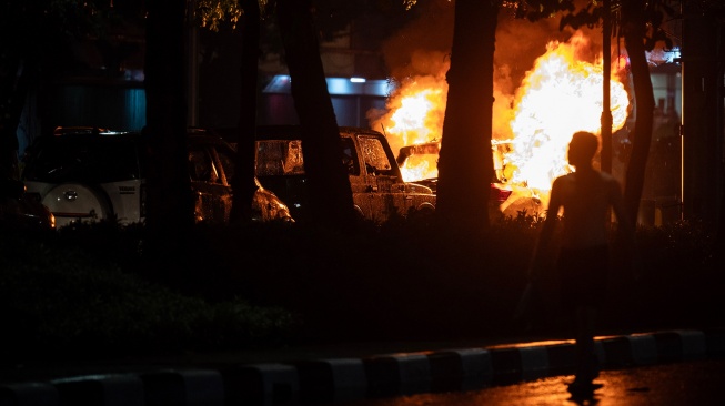 Pengunjuk rasa berjalan disamping mobil yang terbakar saat aksi unjuk rasa di depan Markas Komando (Mako) Brimob Polda Mtero Jaya, Kwitang, Jakarta, Jumat (29/8/2025)malam. [ANTARA FOTO/Bayu Pratama S/wpa]