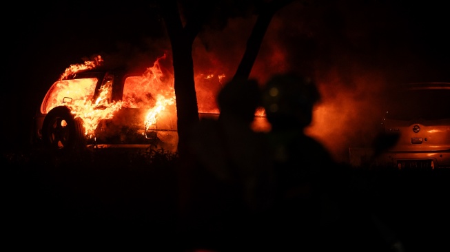 Pengendara motor melintas disamping mobil yang terbakar saat aksi unjuk rasa di depan Markas Komando (Mako) Brimob Polda Mtero Jaya, Kwitang, Jakarta, Jumat (29/8/2025)malam. [ANTARA FOTO/Bayu Pratama S/wpa]