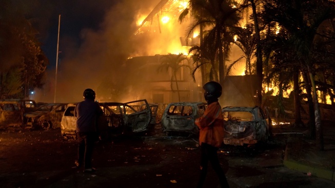 Pengunjuk rasa menyaksikan gedung DPRD Makassar yang telah dibakar di Sulawesi Selatan, Jumat (29/8/2025). [ANTARA FOTO/Hasrul Said/rwa]
