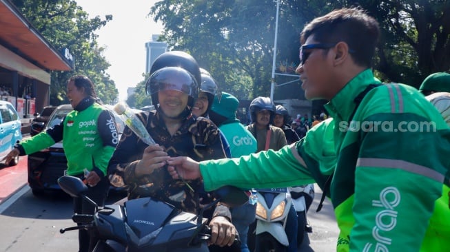 Pengemudi ojek online (ojol) membagikan bunga ke pengguna jalan saat aksi damai di Jalan Merdeka Selatan, Jakarta, Selasa (2/9/2025). [Suara.com/Alfian Winanto]