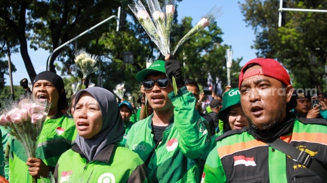 Pengemudi ojek online (ojol) membagikan bunga ke pengguna jalan saat aksi damai di Jalan Merdeka Selatan, Jakarta, Selasa (2/9/2025). [Suara.com/Alfian Winanto]