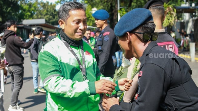 Pengemudi ojek online (ojol) membagikan bunga ke polisi saat aksi damai di Jalan Merdeka Selatan, Jakarta, Selasa (2/9/2025). [Suara.com/Alfian Winanto]