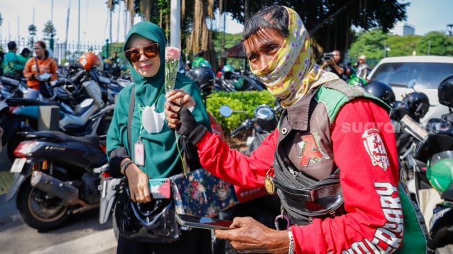 Pengemudi ojek online (ojol) membagikan bunga ke pengguna jalan saat aksi damai di Jalan Merdeka Selatan, Jakarta, Selasa (2/9/2025). [Suara.com/Alfian Winanto]