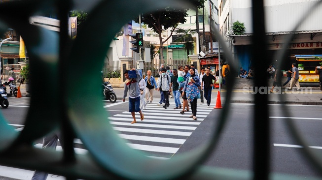Pejalan kaki menyeberang pada pelican crossing di depan Stasiun Cikini, Jakarta, Senin (15/9/2025). [Suara.com/Alfian Winanto]