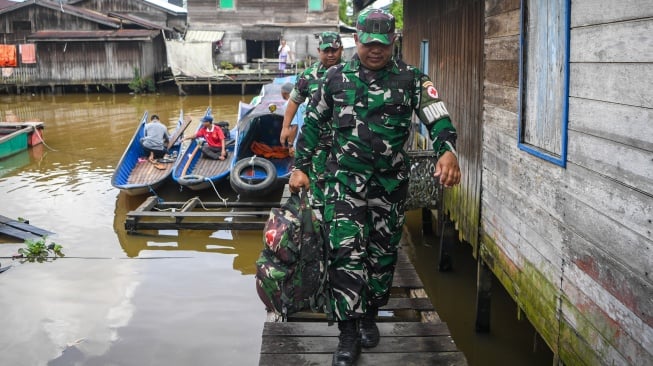 Prajurit TNI AD anggota Kodim 0906/Kutai Kartanegara, Peltu Suhendro (depan) didampingi Babinsa Loa Ipuh Serda Eri Yudin Robiyanto (belakang) berjalan dari perahu klinik terapung saat akan melakukan pemeriksaan kesehatan warga di kawasan Loa Ipuh, Tenggarong, Kutai Kartanegara, Kalimantan Timur, Jumat (19/9/2025). [ANTARA FOTO/M Risyal Hidayat/tom]