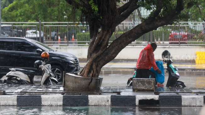 Pengendara berteduh dan memakai jas hujan saat hujan di Kawasan Slipi, Jakarta, Senin (29/9/2025). [Suara.com/Alfian Winanto]