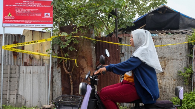 Warga menaiki sepeda listrik saat melintas di dekat plang pengawasan kerawanan bahaya radiasi yang terpasang di lokasi ditemukannya cemaran Cesium-137 (Cs-137) di Kawasan Industri Modern Cikande, Kabupaten Serang, Banten, Kamis (2/10/2025). [ANTARA FOTO/Angga Budhiyanto/nym]