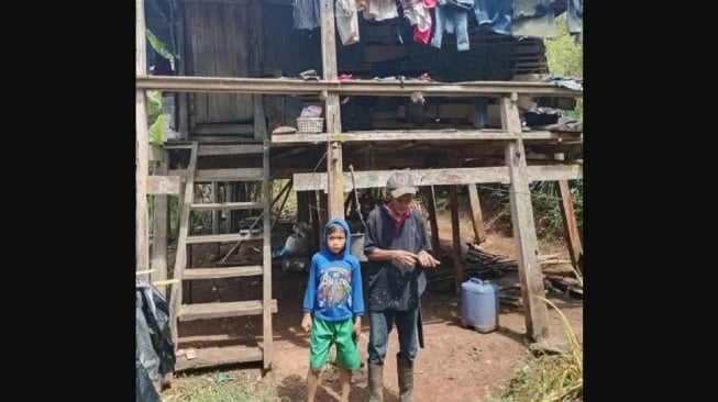 Rangga, Pelajar di SD Inpres Borongbulo, Kecamatan Bontolempangan, Kabupaten Gowa, Sulawesi Selatan berdiri depan rumah panggung bersama kakeknya. Kisah Rangga viral di media sosial [Suara.com/Istimewa]