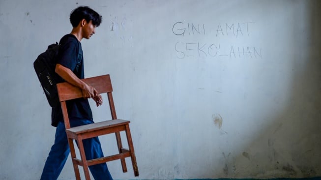 Siswa mengangkat kursi di samping coretan pada dinding kelas di SMK Al-Anshor, Legok, Kabupaten Tangerang, Banten, Selasa (21/10/2025). [ANTARA FOTO/Putra M. Akbar/rwa]