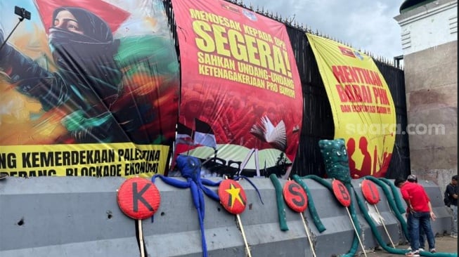 Massa Kongres Aliansi Serikat Buruh Indonesia (KASBI) memasang spanduk besar saat menggelar unjuk rasa di depan Gedung DPR RI. (Suara.com/Faqih)