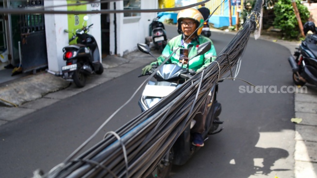 Warga beraktivitas di dekat jaringan kabel utilitas yang menjuntai di kawasan Setiabudi, Jakarta, Rabu (12/11/2025). [Suara.com/Alfian Winanto]