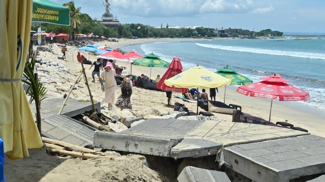 Wisatawan berjalan di dekat jalur pejalan kaki yang rusak di Pantai Kuta, Badung, Bali, Rabu (12/11/2025). [ANTARA FOTO/Fikri Yusuf/rwa]