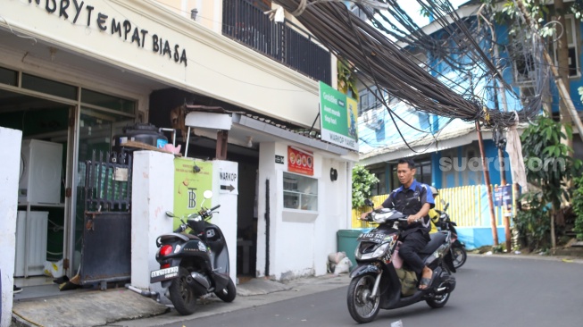 Warga beraktivitas di dekat jaringan kabel utilitas yang menjuntai di kawasan Setiabudi, Jakarta, Rabu (12/11/2025). [Suara.com/Alfian Winanto]
