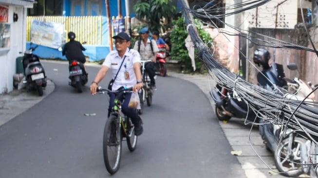 Warga beraktivitas di dekat jaringan kabel utilitas yang menjuntai di kawasan Setiabudi, Jakarta, Rabu (12/11/2025). [Suara.com/Alfian Winanto]