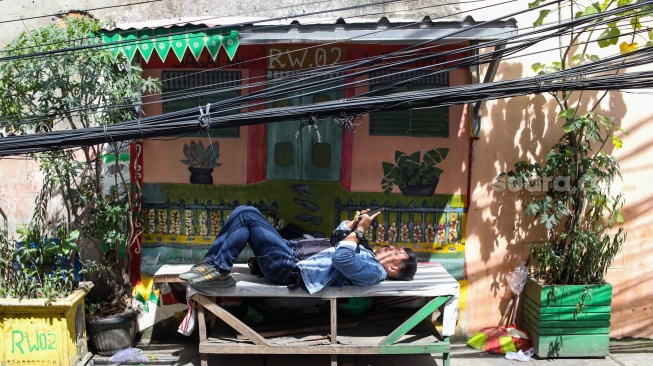 Warga beraktivitas di dekat jaringan kabel utilitas yang menjuntai di kawasan Setiabudi, Jakarta, Rabu (12/11/2025). [Suara.com/Alfian Winanto]
