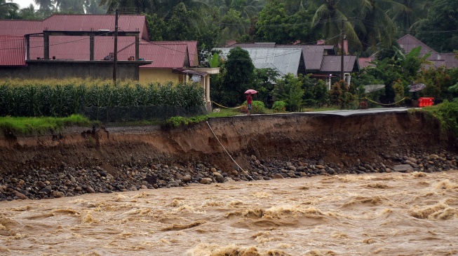 Warga berada di tepi jalan penghubung antar desa yang longsor akibat luapan sungai di Nagari Salibutan, Lubuk Alung, Padang Pariaman, Sumatera Barat, Selasa (25/11/2025). [ANTARA FOTO/Iggoy el Fitra/bar]
