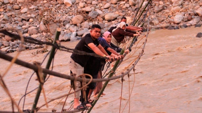 Sejumlah warga melintasi jembatan alternatif yang menghubungkan Desa Blang Meurandeh dan Desa Blang Puuk Beutong Ateuh Banggalang, Nagan Raya, Aceh, Minggu (30/11/2025). [ANTARA FOTO/Syifa Yulinnas/nz]