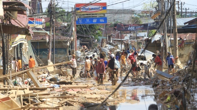 Sejumlah warga melintas di dekat puing-puing yang terbawa arus banjir di kawasan Desa Bukit Tempurung, Kota Kuala Simpang, Kabupaten Aceh Tamiang, Aceh, Rabu (3/12/2025). [ANTARA FOTO/Syifa Yulinnas/nz]
