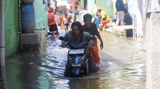 Warga mendorong kendaraannya yang mogok saat melintasi banjir rob di Muara Angke, Jakarta, Jumat (5/12/2025). [Suara.com/Alfian Winanto]