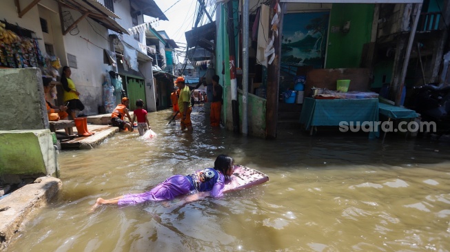 Pengguna jalan melintasi banjir rob di Muara Angke, Jakarta, Jumat (5/12/2025). [Suara.com/Alfian Winanto]