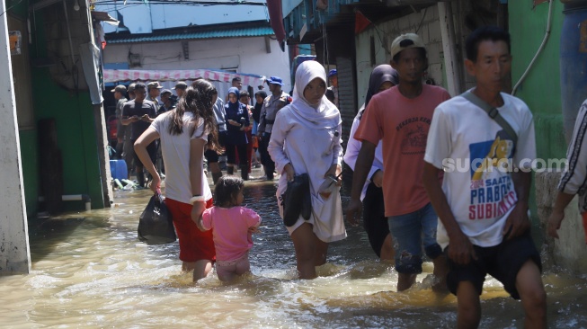 Pengguna jalan melintasi banjir rob di Muara Angke, Jakarta, Jumat (5/12/2025). [Suara.com/Alfian Winanto]