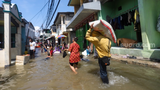 Pengguna jalan melintasi banjir rob di Muara Angke, Jakarta, Jumat (5/12/2025). [Suara.com/Alfian Winanto]