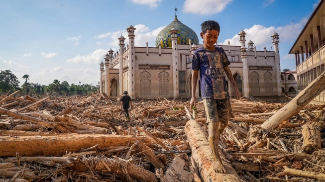 Seorang bocah berjalan meniti kayu-kayu yang memenuhi area Pondok Pesantren Darul Mukhlishin pascabanjir bandang di Desa Tanjung Karang, Karang Baru, Kabupaten Aceh Tamiang, Aceh, Jumat (5/12/2025). [ANTARA FOTO/Erlangga Bregas Prakoso/app/foc]
