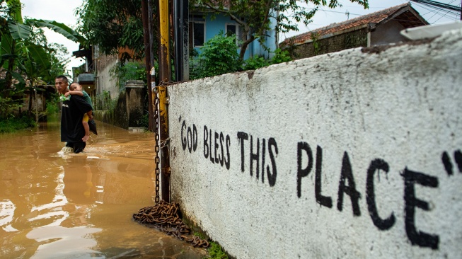 Warga menggendong anaknya saat melintasi banjir di Baleendah, Kabupaten Bandung, Jawa Barat, Sabtu (6/12/2025). [ANTARA FOTO/Novrian Arbi/foc]