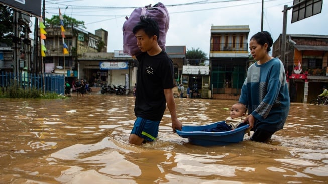 Warga membawa bayinya menggunakan ember saat melintasi banjir di Jalan Raya Dayeuhkolot, Kabupaten Bandung, Jawa Barat, Sabtu (6/12/2025). [ANTARA FOTO/Novrian Arbi/foc]